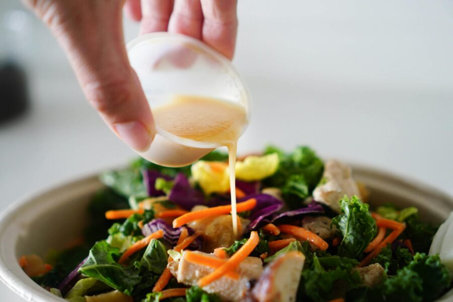 close up photo of a person pouring salad dressing into vegetables