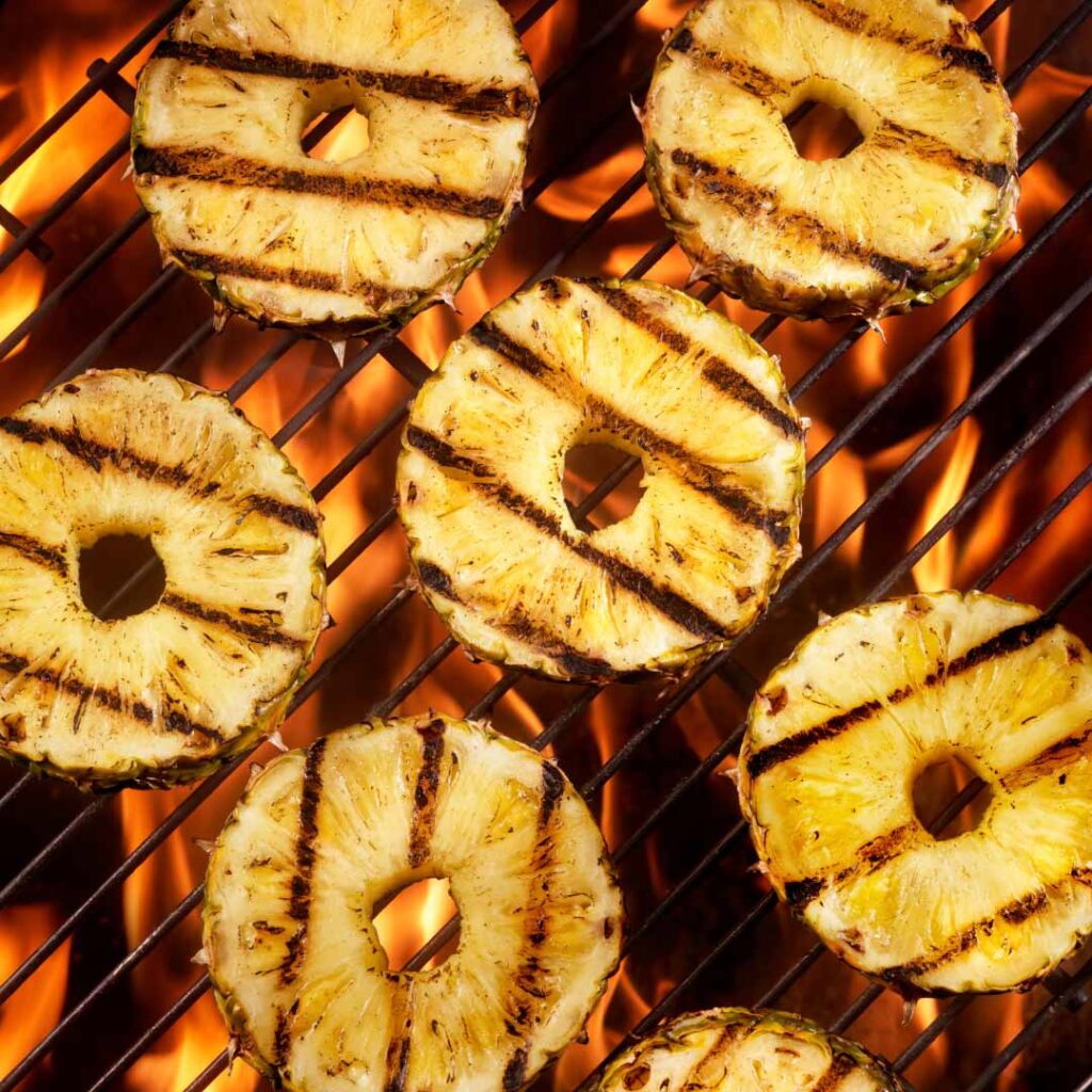 Slices of pineapple with grill marks on a wood fire grill.